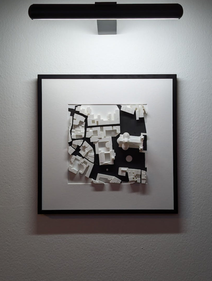 Framed black and white abstract artwork illuminated by a wall-mounted light fixture.